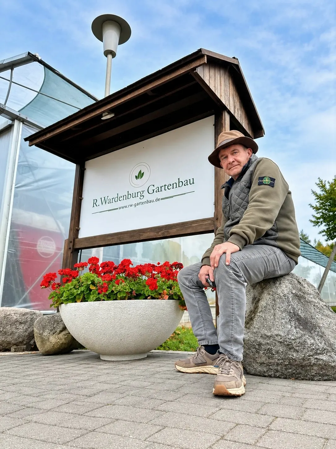 Renke Wardenburg sitzt vor dem Schild seines Betriebs R. Wardenburg Gartenbau.